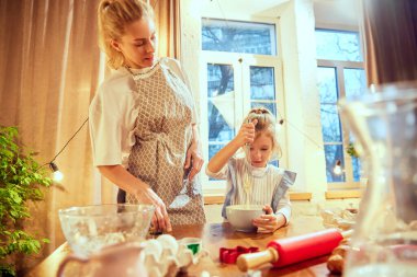 Anne ve küçük kız mutfakta birlikte yemek pişiriyorlar. Küçük kız para kazanıyor, annesi ona yemek yapmayı öğretiyor. Kurabiye günü kavramı, annelik, çocukluk, tatiller, aile