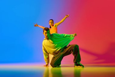 Yetenekli, sanatsal, modern giysiler içinde, neonlu kırmızı arka planda hip hop dansı yapan genç erkek ve kadın. Hobi, eylem, sokak tarzı, modern dans, gençlik, moda kavramı