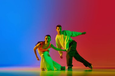 Koordineli hareketler. Genç adam ve kadın, hareketli sokak dansçıları, neonlu mavi arka planda hip hop dansı yapıyorlar. Hobi, eylem, sokak tarzı, modern dans, gençlik, moda kavramı