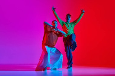 Modern tarz. Genç sanatçı erkek ve kadın hareketli, neon ışıkta pembe arka planda hip hop dansı yapıyorlar. Hobi, eylem, sokak tarzı, modern dans, gençlik, moda kavramı