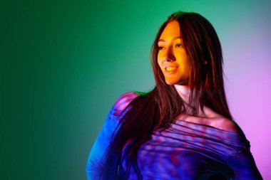 Güzel bir genç kadın, yüz ve vücutta neon yansıması olan değişken pembe arka plana karşı poz veriyor. Sanat anlayışı, modern tarz, siber punk, fütürizm ve yaratıcılık