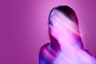 Açık mor arka planda neon ışıklarda poz veren genç bir kızın portresi. Karışık ışık efektleri. Siluet. Sanat anlayışı, modern tarz, siber punk, fütürizm ve yaratıcılık
