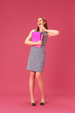 Mutlu, neşeli, gülümseyen genç bir kız. Kitapları ve defterleri pembe stüdyo geçmişine karşı. Heyecan. Gençlik kavramı, insani duygular, eğitim, yaşam tarzı, moda
