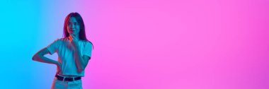 Gradyan pembe mavi stüdyo arka planında neon ışıkta poz veren genç bir kadının portresi. İnsan duyguları, yaşam tarzı, gençlik kültürü, yüz ifadesi kavramı. Pankart. Metin eklemek için boş boşluk