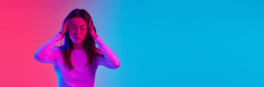 El ele tutuşan genç bir kadın, stresten ve baş ağrısından muzdarip, neon ışıklarındaki pembe renkli stüdyo arkaplanı yüzünden. İnsan duyguları kavramı, yaşam tarzı, gençlik kültürü, yüz ifadesi
