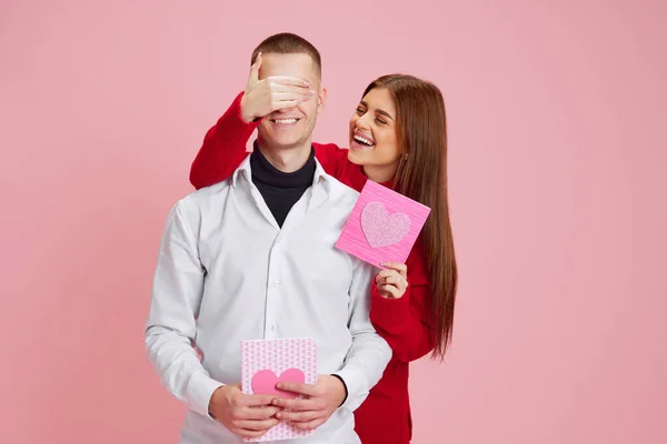 年轻姑娘捂住男朋友的眼睛 带着小礼物送给他 明信片上有粉红色的背景 爱的概念 情人节 生活方式 — 图库照片