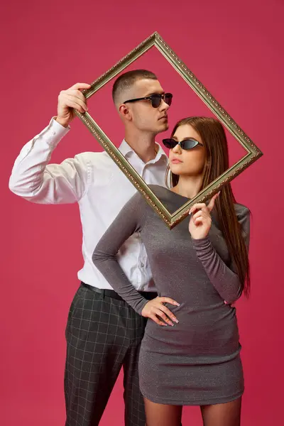 ピンクのスタジオの背景に画像フレームをポーズするサングラスの若いカップル 男と女性 ボンディング バレンタインデー ライフスタイルの概念 — ストック写真
