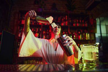 Barda çalışan genç ve güzel bir kız. Lezzetli kokteyller yapıyor. Kadın buzları karıştırıyor, cin bahçesini hazırlıyor. İş kavramı, gece hayatı, bar, parti, alkol içeceği, mixolog