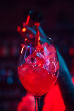 Buzlu cama odaklan ve zencefilden Aperol dök. Neon renkli barda nefis Aperol Spritz kokteyli yapıyorum. Meslek kavramı, gece hayatı, bar, parti, alkol içeceği, mixolog