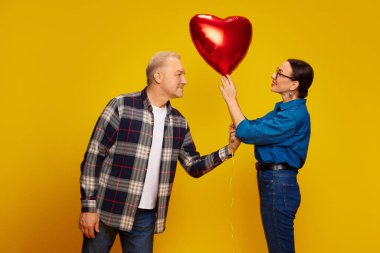 Güzel, mutlu, son sınıf çifti, romantik bayramı kutlayan erkek ve kadın, sarı arka planda kalp şeklinde balon tutuyorlar. Evlilik kavramı, ilişki, Sevgililer Günü, aşk, duygular