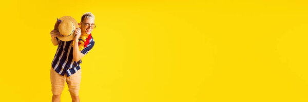 Счастливый молодой блондин в повседневной одежде выбирает соломенную шляпу с улыбкой на фоне жёлтой студии. Концепция человеческих эмоций, молодости, летних каникул, моды. Баннер. Пустое место для ввода текста
