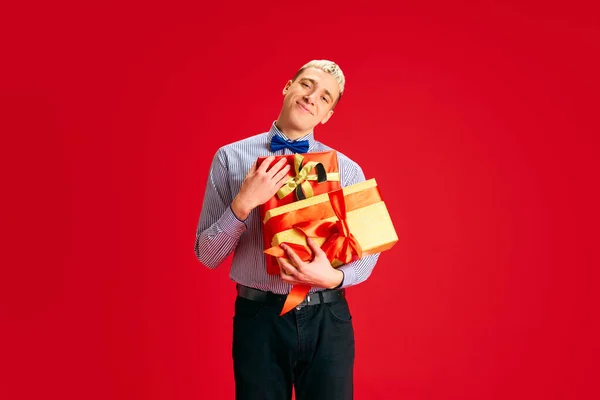赤いスタジオの背景に多くのプレゼントを保持している幸せな笑顔の若者の肖像画 お祝いする 人間の感情 クリスマス 冬休み 休暇の概念 — ストック写真
