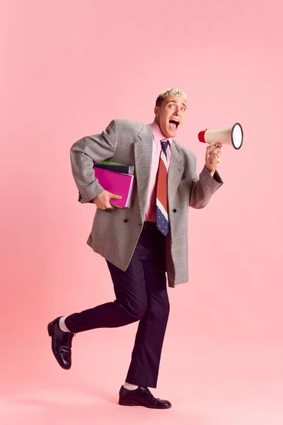 Business tasks. Young guy in formal wear emotionally shouting in megaphone against pink studio background. Concept of emotions, business, profession and occupation, lifestyle