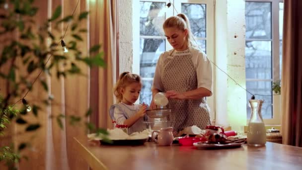 妈妈和小女儿在厨房里一起做饭 小女孩在筛面 妈妈教她做饭 寒假饼干日 家庭的概念 — 图库视频影像
