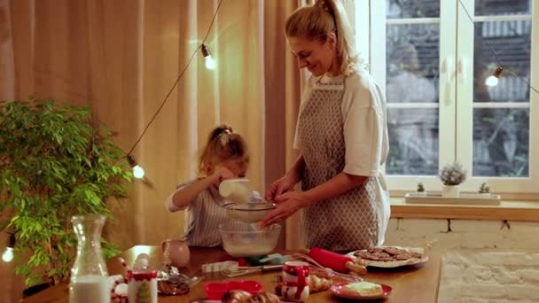 照料她的母亲教她的小女儿做饭 女人和女孩站在家里厨房里做饼干 女人在挑食面粉饼干日 家庭的概念 — 图库视频影像
