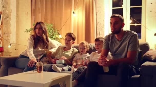 ショックな映画の瞬間 リビングルームでソファーに座ってテレビを見ている家族 感情を表現する 家族のコンセプト レジャー時間 リラクゼーション 幼少期 親として — ストック動画