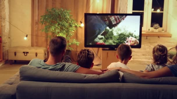 両親と子供たちが一緒に夜を過ごし リビングルームでソファーに座ってテレビを見たり 軽食を食べたりする様子を背景にした 家族のコンセプト レジャー時間 リラクゼーション 幼少期 親として — ストック動画