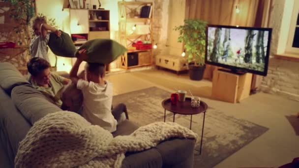 孩子们 兄弟们和小妹坐在客厅的沙发上 一起看电视 吃小吃 玩的开心 闲暇时间 为人父母的概念 — 图库视频影像