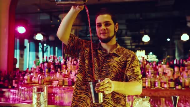 笑容满面的年轻人 酒保做甜甜的鸡尾酒 含笑的液体与震动 尼昂彩色吧 夜生活 酒保工作的概念 — 图库视频影像