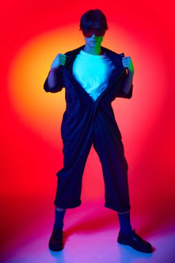 Tulumlu ve koruyucu gözlüklü yakışıklı bir gencin renkli arkaplan ışıklarıyla tam boy portresi. Gençlik kültürü, moda ve erkek güzelliği, duygular, ilham, eğilimler kavramı