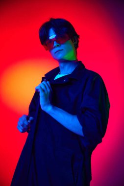 Tulumlu ve koruyucu gözlüklü yakışıklı bir gencin portresi renkli arka planda neon ışıkta. Müsrif moda. Gençlik kültürü kavramı, erkek güzelliği, duygular, ilham, eğilimler