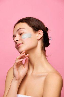 Duşta pembe arka planda duran yüzü maskeli güzel, hassas genç bir kız. İçecek bir şeyler. Doğal kadın güzelliği, cilt bakımı, kozmetik ve kozmetik kavramı