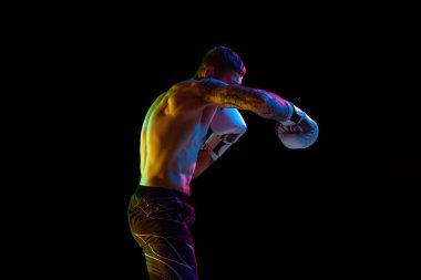 Genç kaslı adam, hareketli boks sporcusu, antrenman, ringde dövüş neon ışıkta siyah arka planda izole edilmiş. Profesyonel spor anlayışı, dövüş sporu, dövüş sanatları, güç