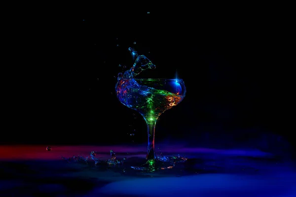 Martini splash. Glass with popular cocktail standing against dark background with neon light with smoke. Concept of alcohol drink, nightclub, party, taste, celebration.