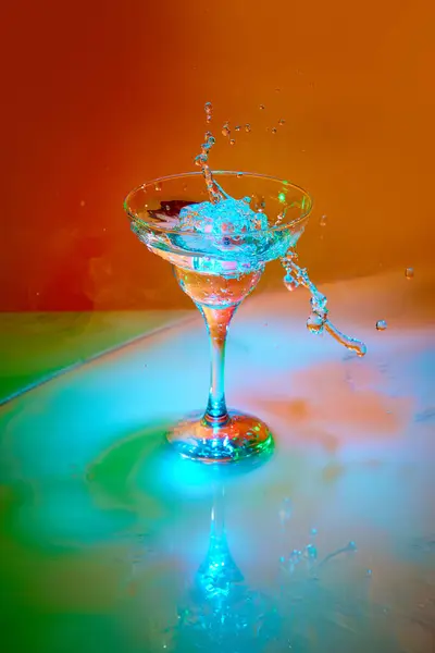 冰块在霓虹灯下与马提尼鸡尾酒一起倒入玻璃杯 呈橙色背景 具有烟熏效果 喝几滴水 酒精饮料 夜总会 庆祝的概念 — 图库照片