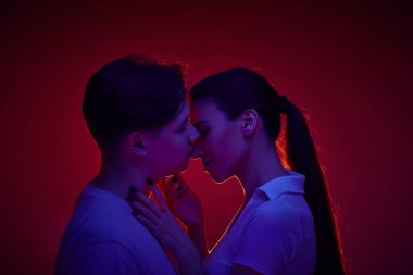 Genç adam ve kadın, mutlu çift öpüşüyor, neon ışıkta kırmızı arka plana karşı sevgi ve ilgi gösteriyorlar. Romantizm, aşk, ilişki, tutku, gençlik, flört, mutluluk kavramı