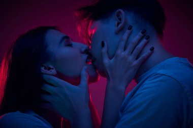 Tutkulu genç erkek ve kadın portresi, öpüşen çift, neon ışıkta mor arka plana karşı aşkı ifade ediyor. Romantizm, aşk, ilişki, tutku, gençlik, flört, mutluluk kavramı
