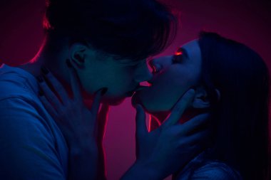 Romantik, sevgi dolu, şefkatli genç bir kadın ve erkek. Mor arka planda öpüşen bir çift. Romantizm, aşk, ilişki, tutku, gençlik, flört, mutluluk kavramı