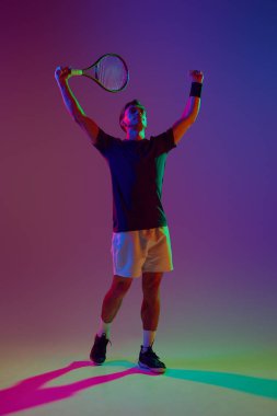 Kazanan, şampiyon. Tenisçi raketle ayakta duruyor, Neon 'un gradyan stüdyo geçmişine karşı kazandığımız maçı kutluyor. Profesyonel spor, rekabet, oyun, matematik, hobi, eylem kavramı