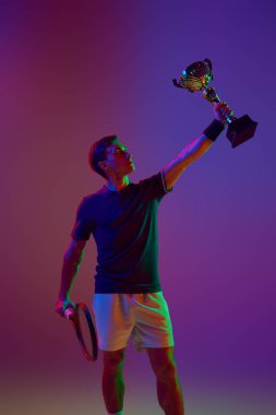 Kazanan, şampiyon. Tenisçi raketle ayakta duruyor, Neon 'un gradyan stüdyo geçmişine karşı kazandığımız maçı kutluyor. Profesyonel spor, rekabet, oyun, matematik, hobi, eylem kavramı