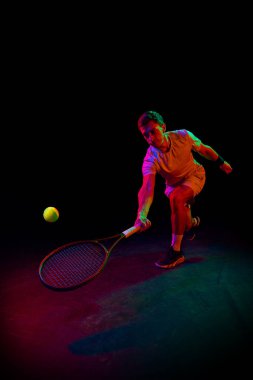 Genç bir adam, oyun sırasında tenis oynuyor, neon ışıkta karanlık arka planda pratik yapıyor. Profesyonel spor, rekabet, oyun, matematik, hobi, eylem kavramı
