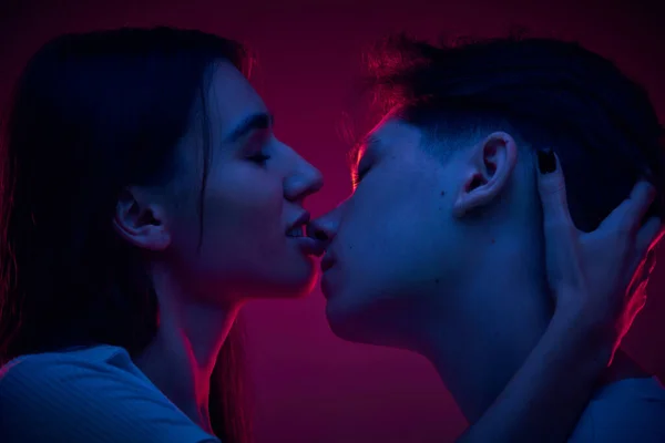 彼女のボーイフレンドにキスするテンダーの若い女性は ネオンライトの紫色の背景に対する愛とケアを示しています ロマンス デート 幸福の概念 — ストック写真