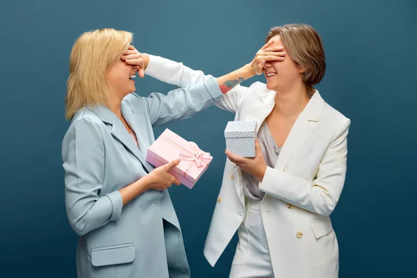 Women Couple Suits Celebrating Holiday Covering Eyes Presenting Gifts Each — Stock Photo, Image