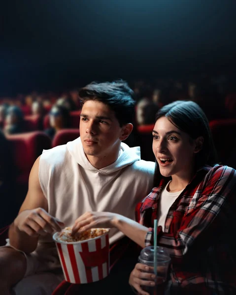 Young man and woman, couple, friends visiting cinema, watching movie with interest and excitement, eating popcorn. Concept of leisure time, relationship, emotions, weekend activity