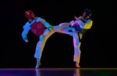 Rekabetçi genç erkekler, tekvando, hareketli karate sporcuları, neon ışıkta siyah arka plana karşı antrenman, kavga. Dövüş sanatları kavramı, dövüş sporu, rekabet, eylem, güç