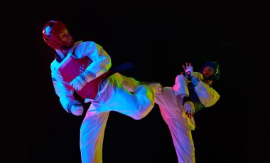 Rekabetçi genç erkekler, tekvando, hareketli karate sporcuları, neon ışıkta siyah arka plana karşı antrenman, kavga. Dövüş sanatları kavramı, dövüş sporu, rekabet, eylem, güç