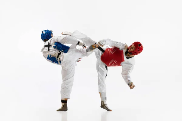 Two men in kimono and helmets practicing taekwondo, training, fighting isolated over white background. Concept of martial arts, combat sport, competition, action, strength, education