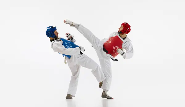 Two men in kimono and helmets practicing taekwondo, training, fighting isolated over white background. Concept of martial arts, combat sport, competition, action, strength, education
