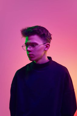 Siyah uzun kollu yakışıklı bir gencin portresi ve neon ışıkta mor arka plana bakıp duran gözlükler. İnsan duyguları kavramı, gençlik, modern tarz, moda