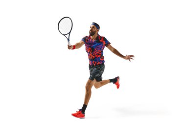 Renkli spor kıyafetleriyle tenis oynayan sakallı genç adam, beyaz arka planda izole edilmiş raketle hareket ediyor. Profesyonel spor, hareket, rekabet, eylem kavramı. Ad