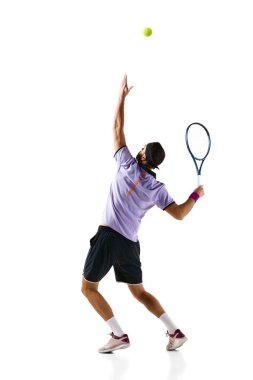 Genç bir adamın tam boy dinamik görüntüsü, hareket halindeki bir tenis oyuncusu, beyaz arka planda izole edilmiş raketle servis yapan bir top. Profesyonel spor, hareket, rekabet, eylem kavramı. Ad