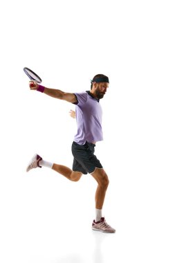 Konsantre rekabetçi genç adam, oyun sırasında hareket eden tenis oyuncusu, beyaz arka planda soyutlanmış olarak oynuyor. Profesyonel spor, hareket, rekabet, eylem kavramı. Ad