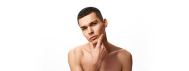Vahşi yüzlü yakışıklı genç adam, temiz tıraşlı ten beyaz stüdyo geçmişine karşı üstsüz duruyor. Erkek güzelliği, cilt bakımı, spa, kozmetoloji, erkek sağlığı kavramı. Pankart. Ad