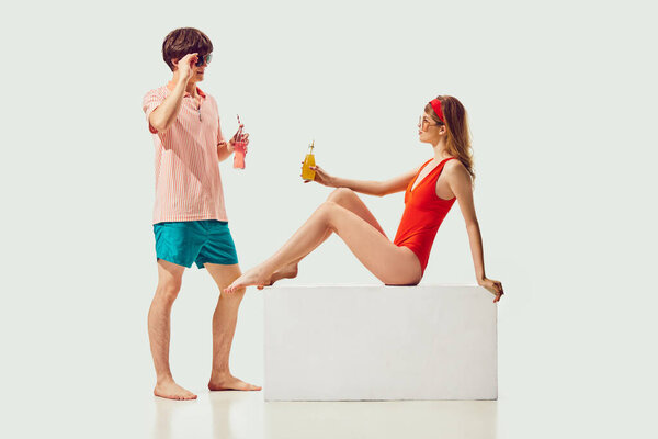 Handsome young man and pretty woman in retro summer clothes, swimsuit looking at each other against white background. Meeting. Concept of summer vacation, travelling, retro style, fashion, love