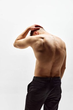 Arkadan dolaş. Beyaz stüdyo arka planında izole edilmiş pantolonla duran kaslı, kaslı, genç bir adam. Sağlık hizmetleri. Erkek güzelliği, vücut bakımı, spor, moda kavramı