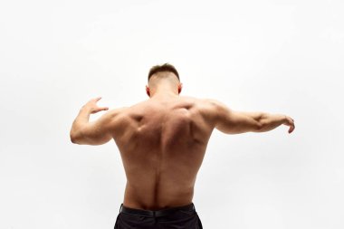 Beyaz stüdyo arka planında izole edilmiş, kaslı vücutlu, sırtı güçlü, gömleksiz erkek modelin dikiz görüntüsü. Erkek güzelliği, vücut bakımı, spor, sağlık